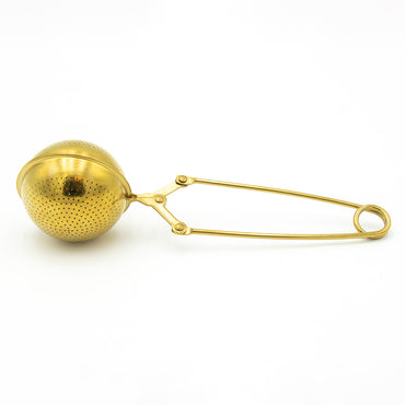 The Gold Scissor Infuser features a perforated gold sphere and a long, hinged handle with a loop, shown elegantly against a white background.