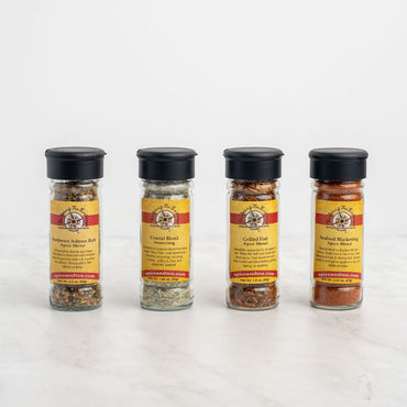 The Seriously Seafood 4-Pack Gift Set features four glass spice jars with black lids, each containing a unique blend. Bright yellow and red labels show names and ingredients—ideal for enhancing your favorite seafood dishes.