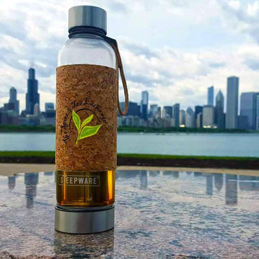 The Urban Tea Tumbler, featuring an eco-friendly design and a cork sleeve, sits on stone with the Chicago skyline and waterfront in the background beneath a cloudy sky, highlighting its modern style.