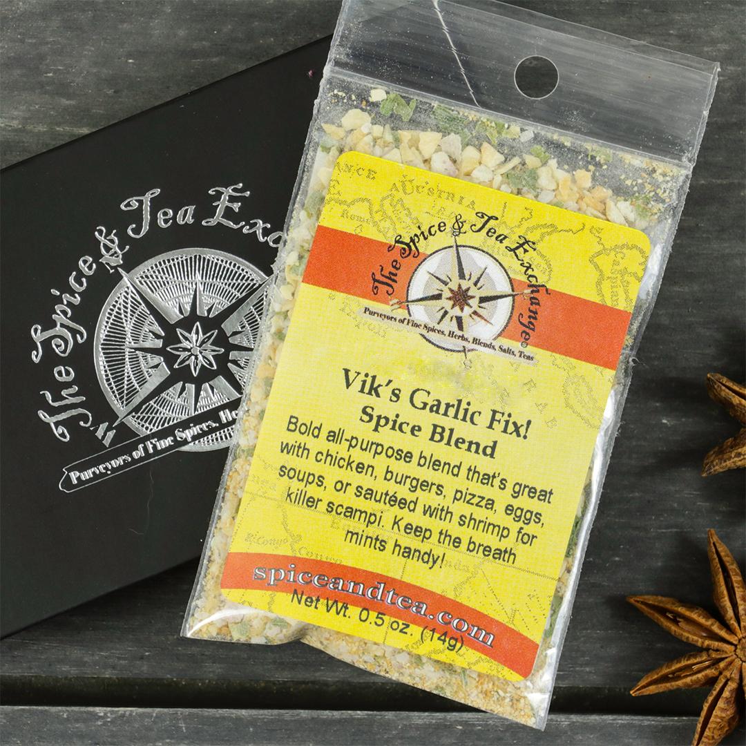 A packet of Vik's Garlic Fix Spice Blend - Barter Box sits on a black branded box with dried star anise nearby. This versatile garlic blend is perfect for enhancing dishes or including in a gift sampler.