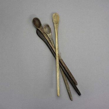 Four Wooden Tasting Spoons in assorted brown shades are fanned out on a plain gray background, highlighting their rustic charm. These essential kitchen tools combine a well-used look with varied natural tones.
