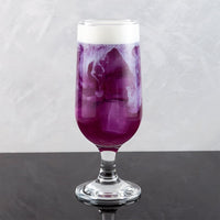 Purple cocktail with white foam in a glass on a gray surface and background