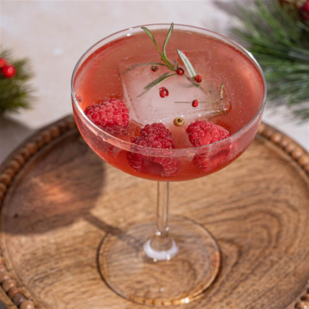 Red cocktail with raspberries and a sprig of rosemary on a wooden tray.