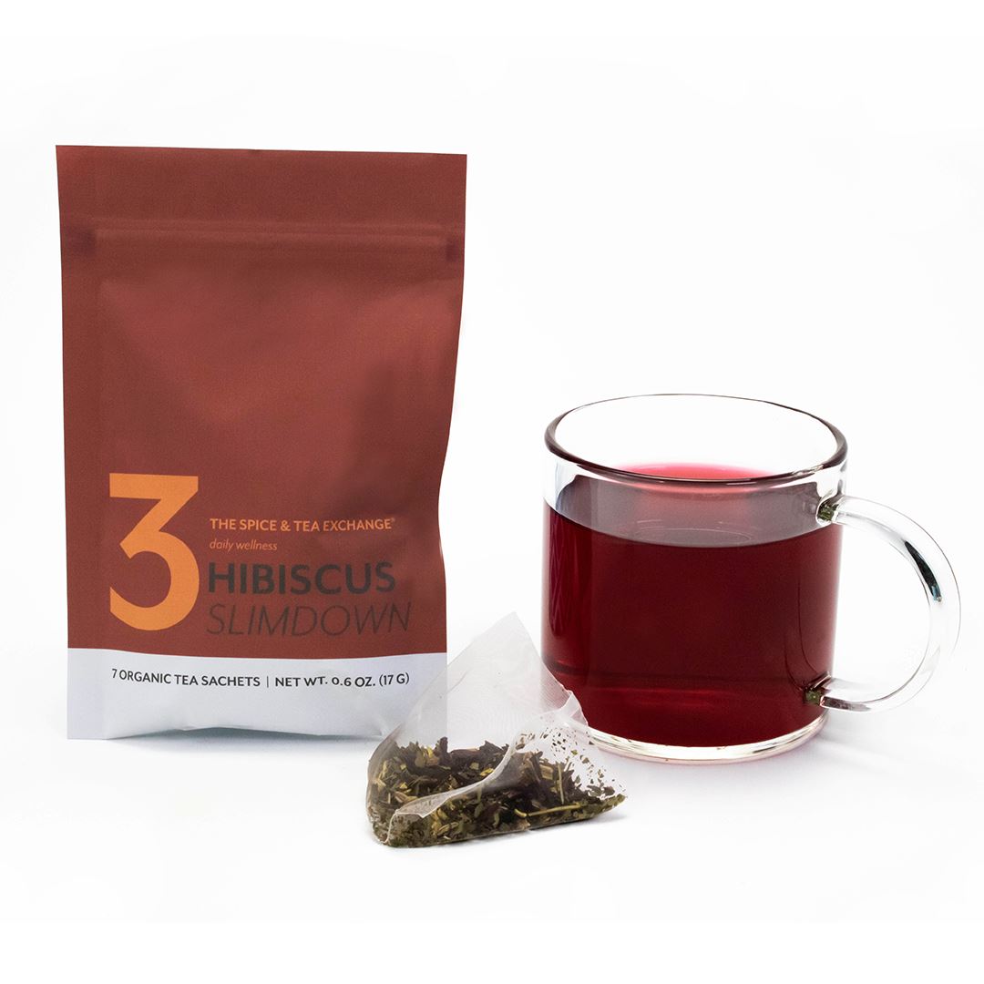A brown packet labeled 7 Day Organic Tea Cleanse sits next to a clear glass mug filled with red tea and a used sachet, illustrating the benefits of wellness teas against a white background.