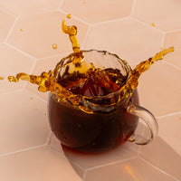Glass mug filled with tea, on a hexagonal tile background.