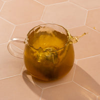 Clear glass teapot filled with a yellowish tea on a beige hexagonal tile background
