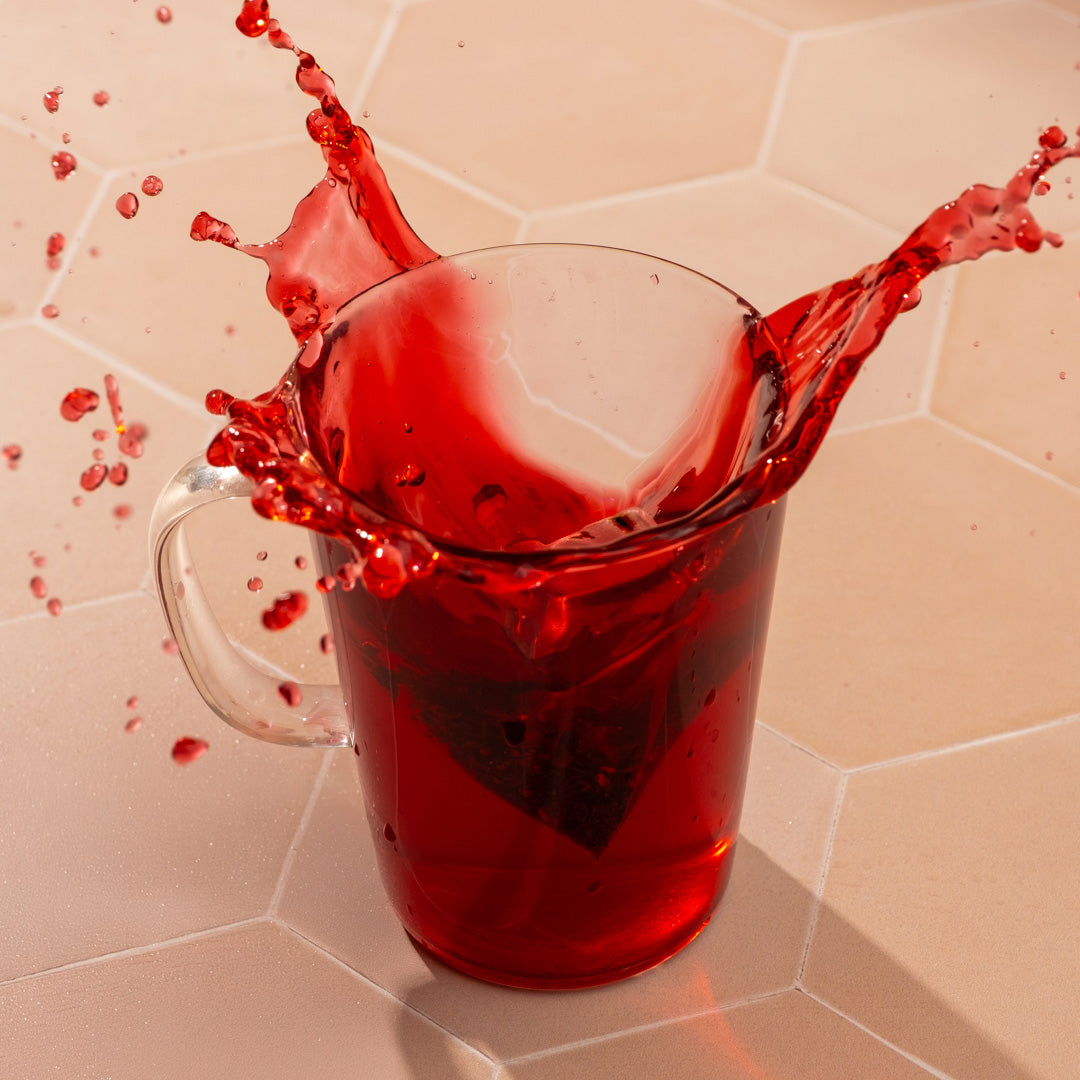 Clear glass mug filled with red tea on a beige tiled surface