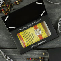 A black box with a window displays the Baker's Spice Blend - Barter Box, an ideal gift for baking enthusiasts. Decorative peppercorns and ribbon are scattered on a dark wooden surface.
