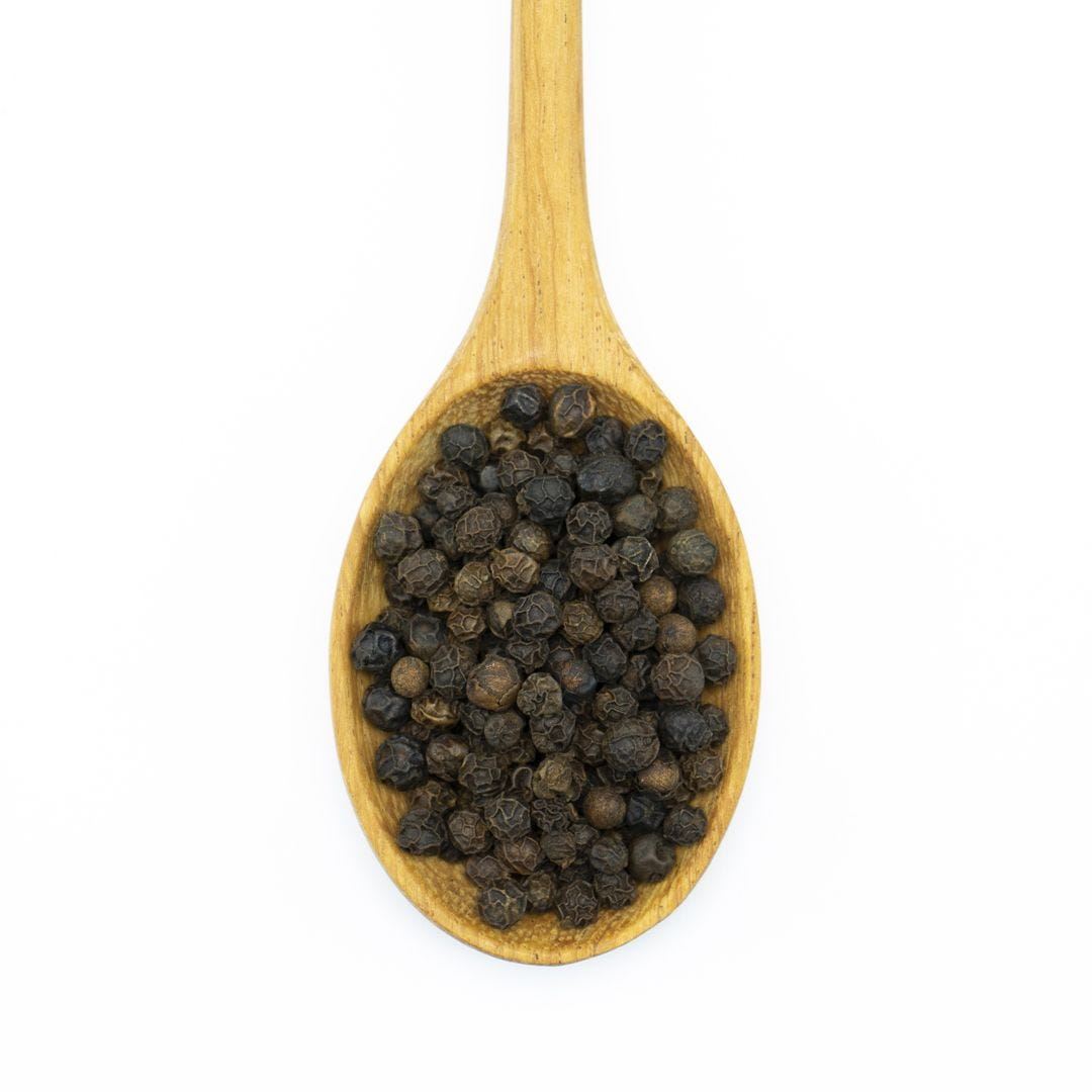 A wooden spoon filled with Smoked Black Peppercorn, photographed on a white background.
