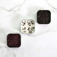 Three small square containers with tea leaves on a marble surface