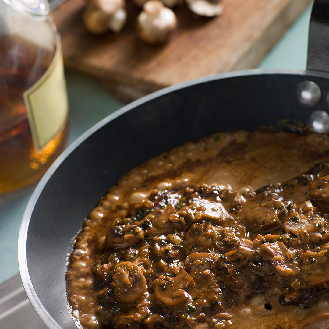 Mushroom sauce in a pan with a bottle of beer on a wooden surface