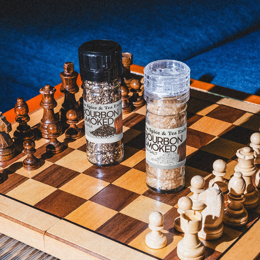 Two bottles of bourbon smoked salt on a chessboard with chess pieces.