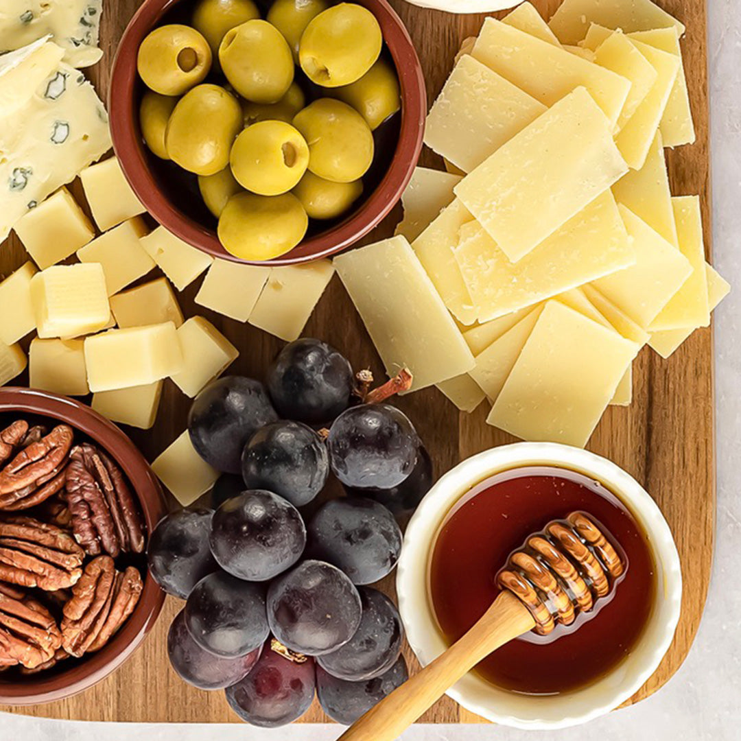 Assorted cheese, olives, grapes, and honey on a wooden board.