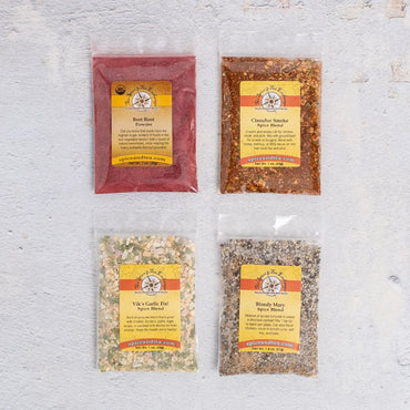 The Burger Seasonings Sampler features four clear packets with yellow labels: Beet Root, Clambake Smoke, Viki's Garlic Hut, and Bloody Mary—each a unique blend perfect for your next grilling night.