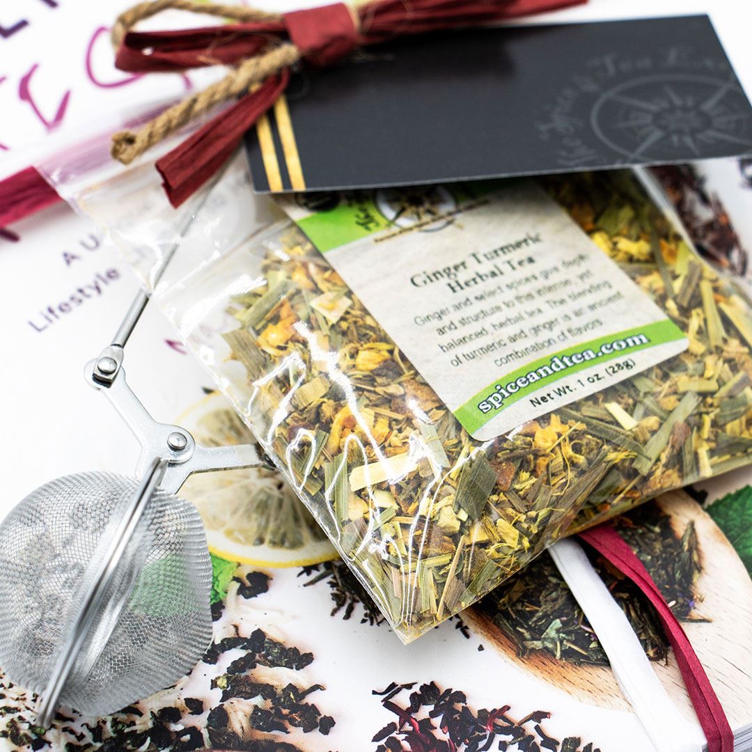 The Cancer Hates Tea Book & Bundle - Ginger Turmeric is shown with a clear bag of herbal tea, metal tea infuser, and gift card, arranged on a vibrant food and tea magazine—ideal for tea lovers and wellness enthusiasts.