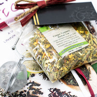 The Cancer Hates Tea Book & Bundle - Ginger Turmeric is shown with a clear bag of herbal tea, metal tea infuser, and gift card, arranged on a vibrant food and tea magazine—ideal for tea lovers and wellness enthusiasts.