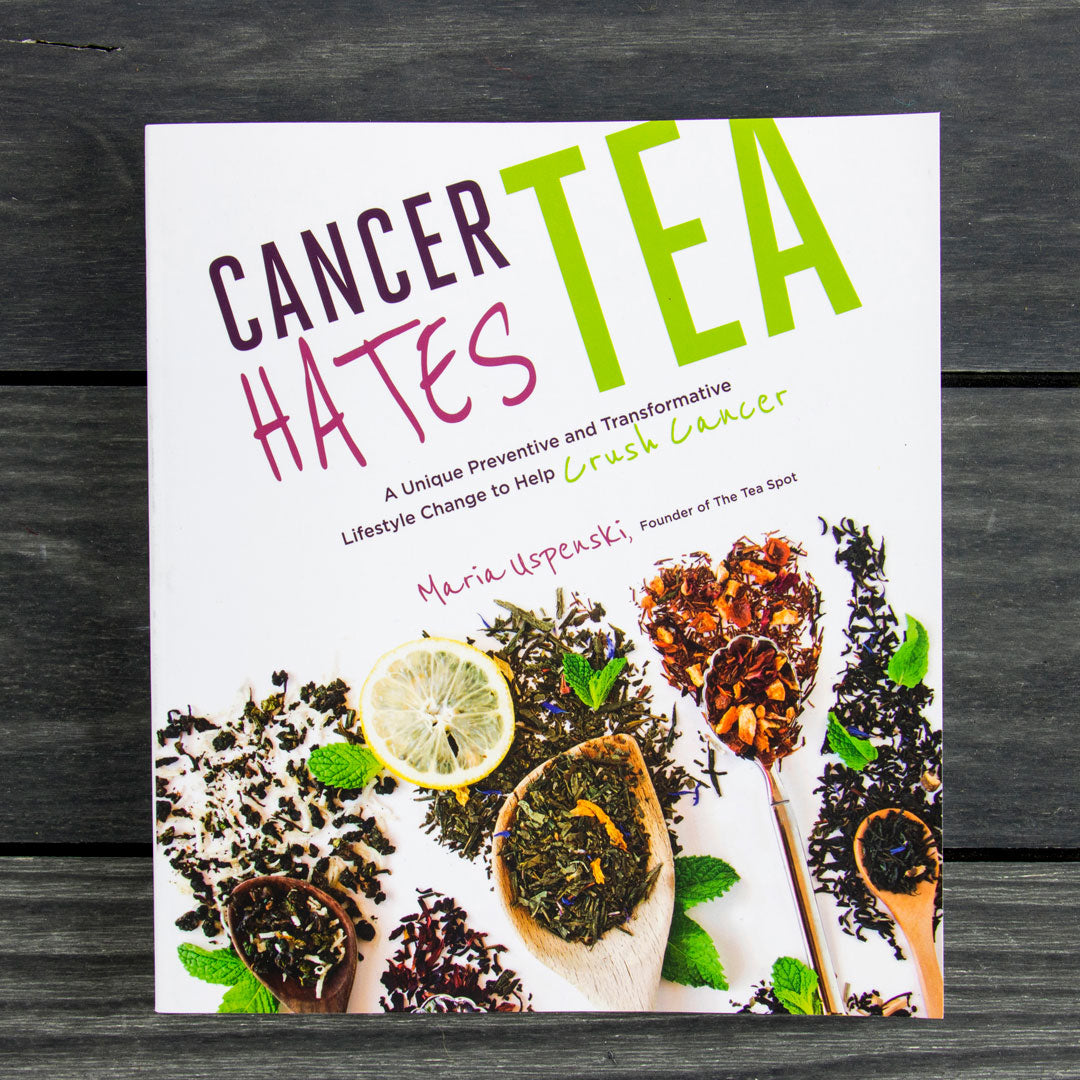 The Cancer Hates Tea Book cover displays vibrant tea leaves, lemon slices, and wooden spoons on a dark wood table with bold title text—ideal for tea lovers or those interested in wellness and cancer awareness.