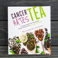 The Cancer Hates Tea Book cover displays vibrant tea leaves, lemon slices, and wooden spoons on a dark wood table with bold title text—ideal for tea lovers or those interested in wellness and cancer awareness.