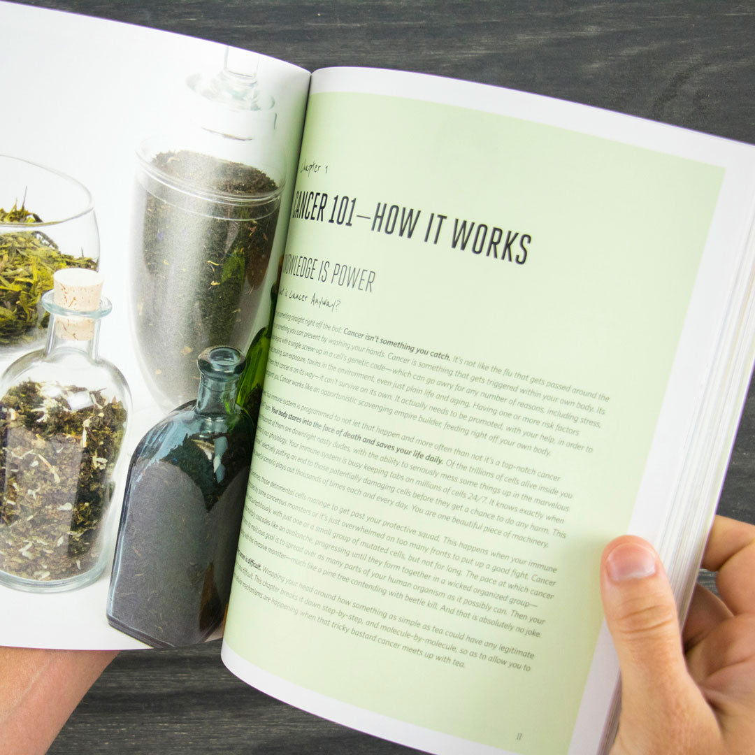 A person holds open the "Cancer Hates Tea Book" to a page titled "Cancer 101—How It Works," showing jars filled with herbs on the left, emphasizing tea and wellness, and text on a light green background on the right.
