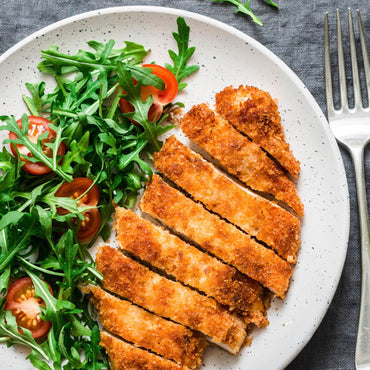 Sliced fried chicken on a plate with a side salad and a fork on a gray surface