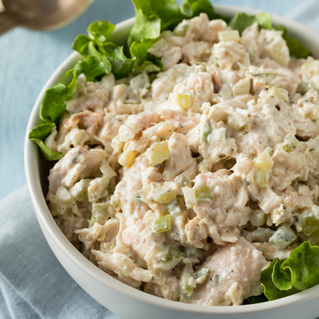 Chicken salad with celery and green leaves in a white bowl on a light blue background