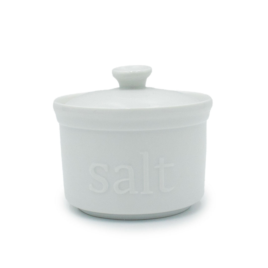 The White Ceramic Salt Cellar features a matching lid and "salt" embossed on the front, ideal for storing artisan salts and adding style to your kitchen storage.