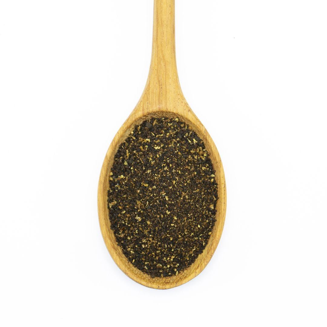 A wooden spoon filled with Dark Chili Powder, photographed from above on a white background.