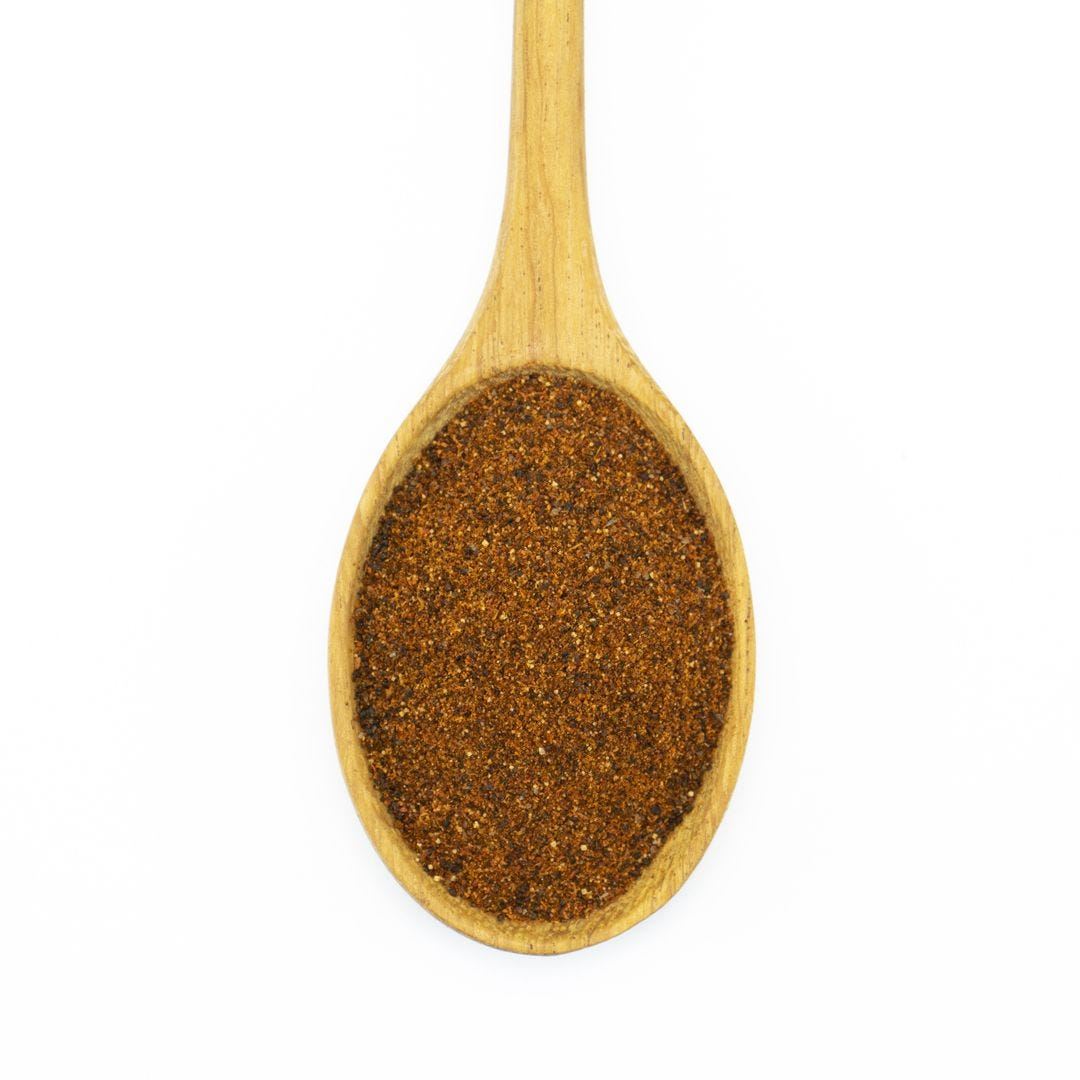A wooden spoon filled with finely ground Light Chili Powder, brownish-red in color, viewed from above against a white background.