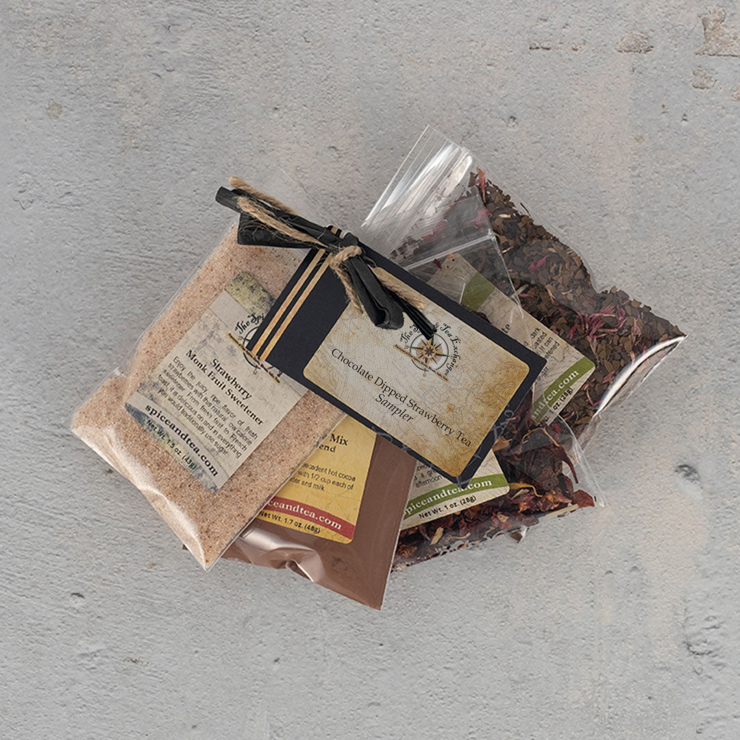 Three clear bags of Chocolate-Dipped Strawberry Tea Sampler, featuring berry bouquet and nutty chocolate mate blends, are tied with black string and labeled cards, displayed on a light gray textured surface.