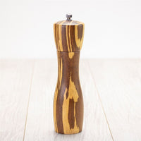 The 8" Crushed Bamboo Pepper Mill, featuring a natural striped wood grain, stands upright on a light wooden surface against a plain white background—an ideal unique kitchen gift.