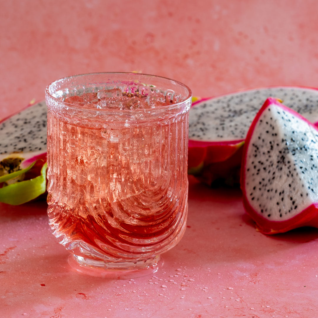 Dragon Fruit Fusion Herbal Tea in a clear glass, iced, next to dragon fruit slices