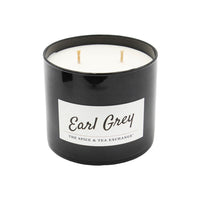 The Earl Grey Candle features a black jar with a white wax interior and three unlit wicks. Infused with essential oils, this natural soy candle from The Spice & Tea Exchange is shown on a white background.