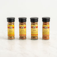 The Fiesta Flavors 4-Pack Gift Box includes four spice jars with black lids and yellow-red striped labels, each containing a different Latin American seasoning from Spice and Tea Co., arranged in a row on a white background.
