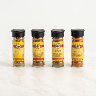 The Fiesta Flavors 4-Pack Gift Box includes four spice jars with black lids and yellow-red striped labels, each containing a different Latin American seasoning from Spice and Tea Co., arranged in a row on a white background.
