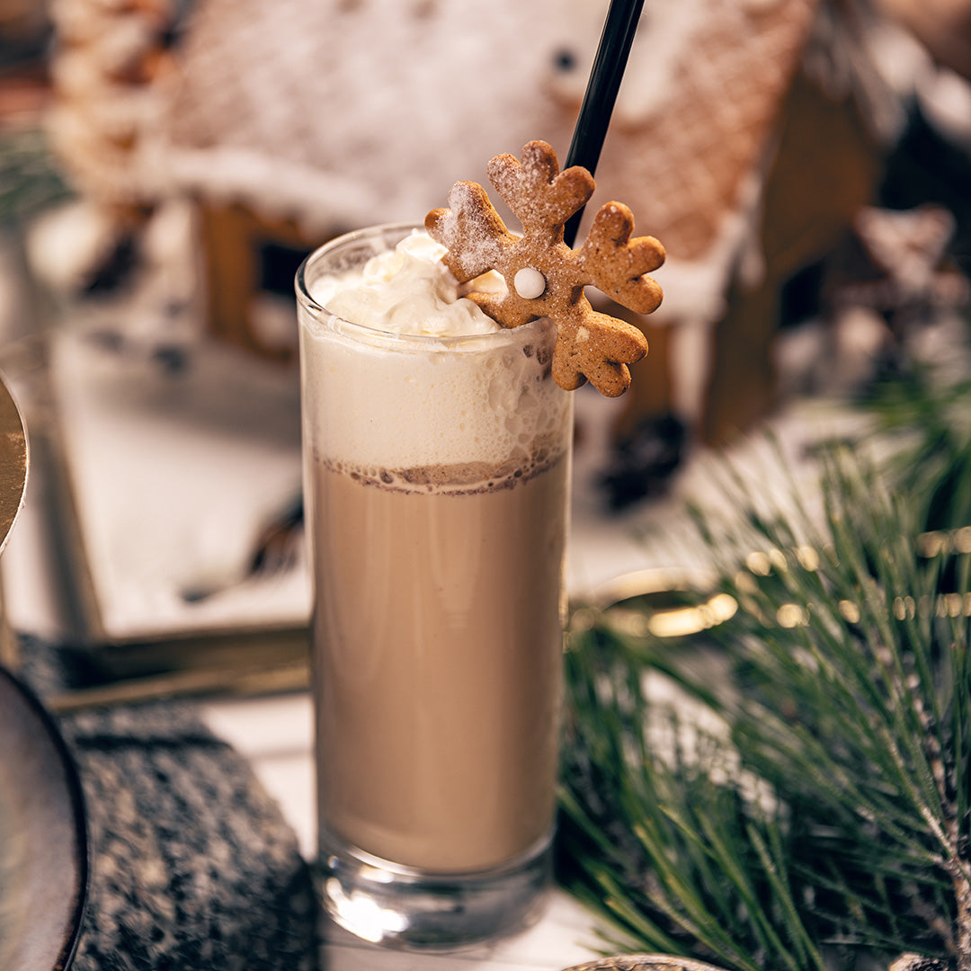 Hot chocolate with whipped cream and a gingerbread cookie in a glass, set against a festive background.