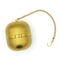 The Gold Ball Infuser - Large features a perforated, oval design with a central seam and metal chain with hook—perfect for steeping loose tea in hot water.
