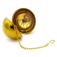 The Gold Ball Infuser - Small is shown open, displaying its two perforated halves with a chain and hook attached. This gold metal tea infuser rests on a white background.