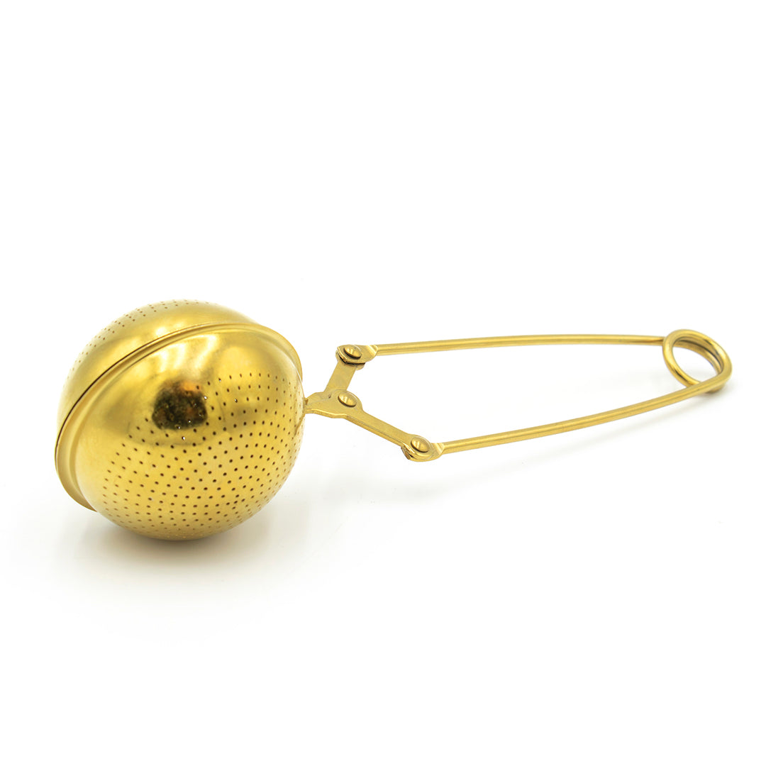 The Gold Scissor Infuser features a gold, round perforated metal ball with a long handle, ideal for holding loose tea leaves while steeping in hot water.