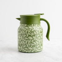 The Green Hot Tea Steeper rests on a white surface, featuring a dense green leaf pattern on its body with a solid green lid, handle, and spout—ideal for brewing loose-leaf tea.