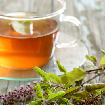 Clear glass mug with tea and green leaves on a wooden surface