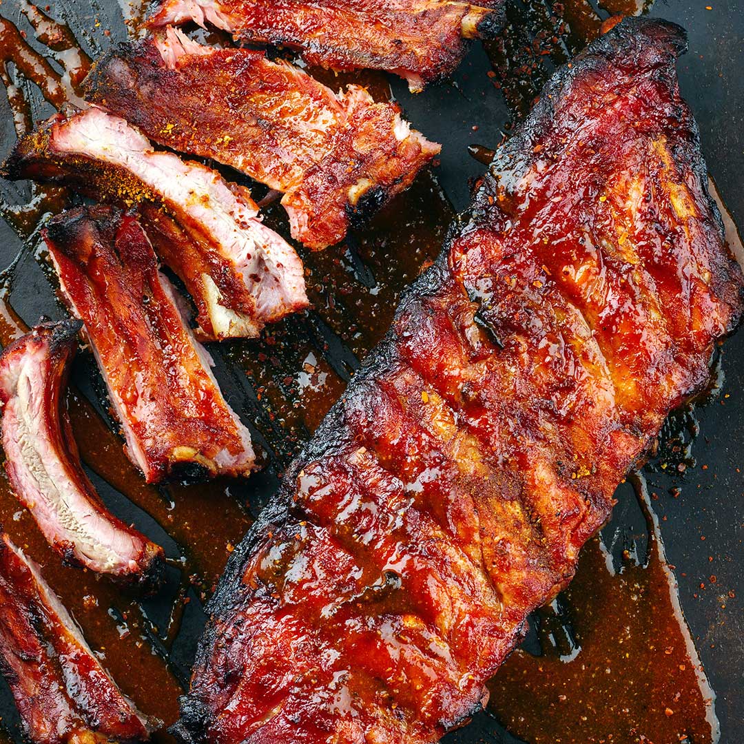 Rack of ribs on charcoal slate covered in red sauce and spice rub