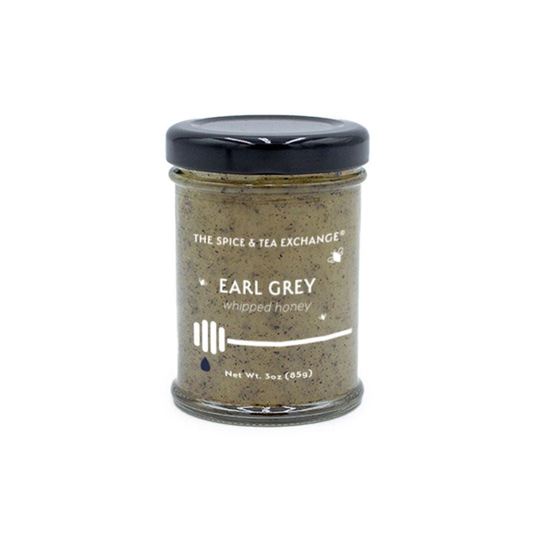 The Earl Grey Whipped Honey Jar from The Spice & Tea Exchange is a 3oz (85g) glass jar with a black lid, featuring creamy natural honey infused with Earl Grey flavor and a honey dipper illustration on the label.