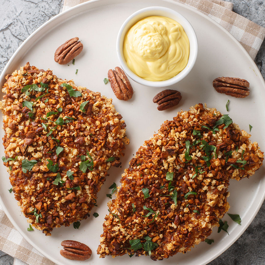 Two pieces of breaded chicken with a side of mustard on a white plate.