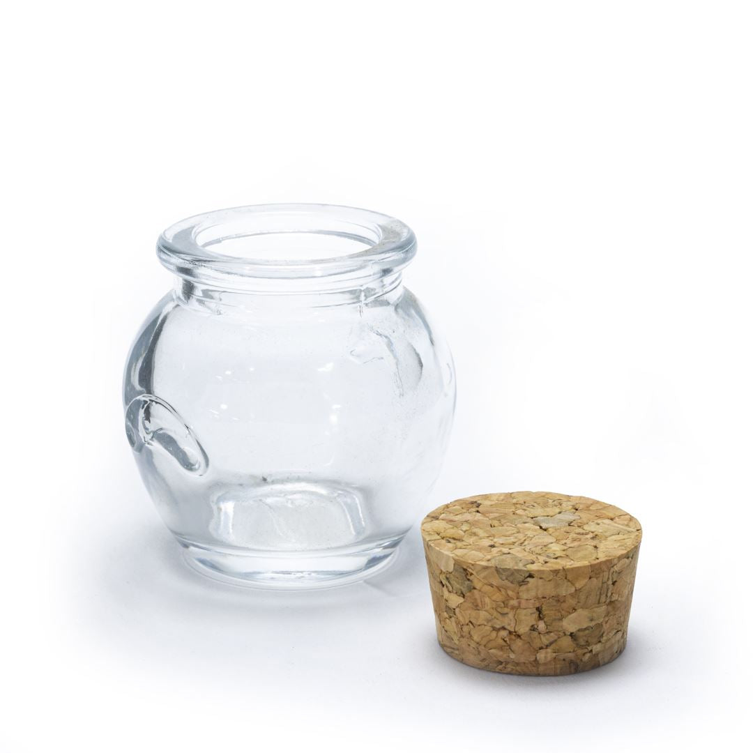 The Glass Jar Honey Pot with Cork, a small round glass jar with a wide opening, sits empty next to its cork lid on a white background—perfect for spice storage.