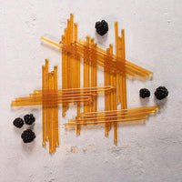 Blackberry Blossom Honey Straws are arranged in a crisscross pattern on a light surface, surrounded by fresh blackberries for a colorful and healthy snack.