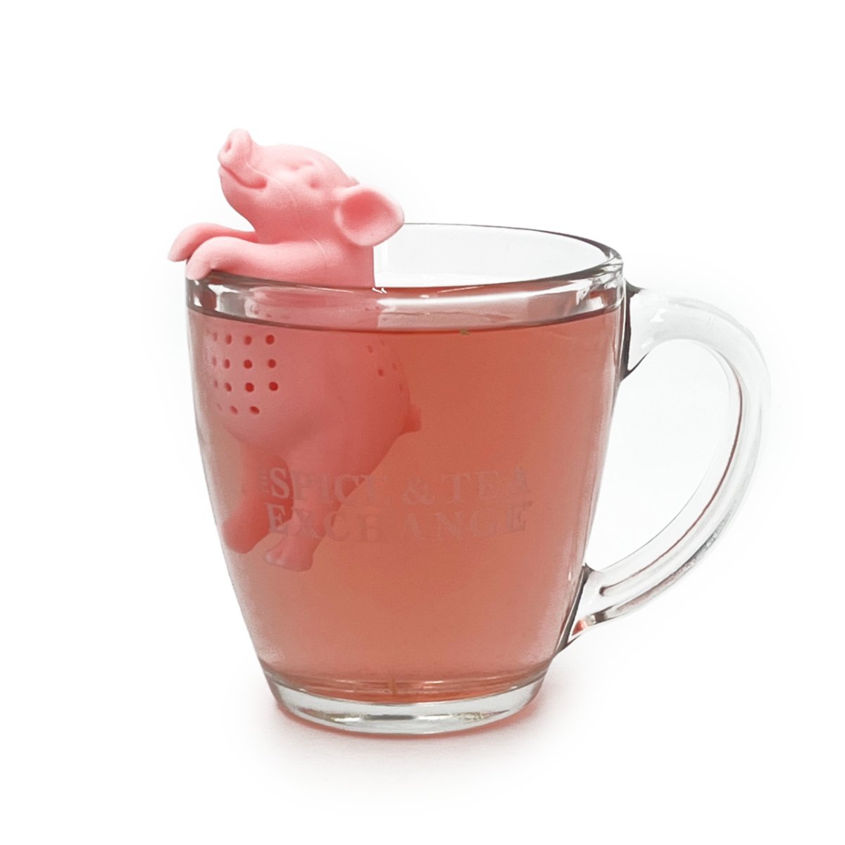 A clear glass mug holds pink tea brewed with the Hot Belly Infuser, a BPA-free silicone pig-shaped tea accessory that hooks over the rim with its head and front legs outside—ideal for making your favorite loose tea.