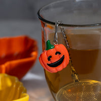 Pumpkin-shaped charm and tea ball infuser  on a glass with a blurred background.