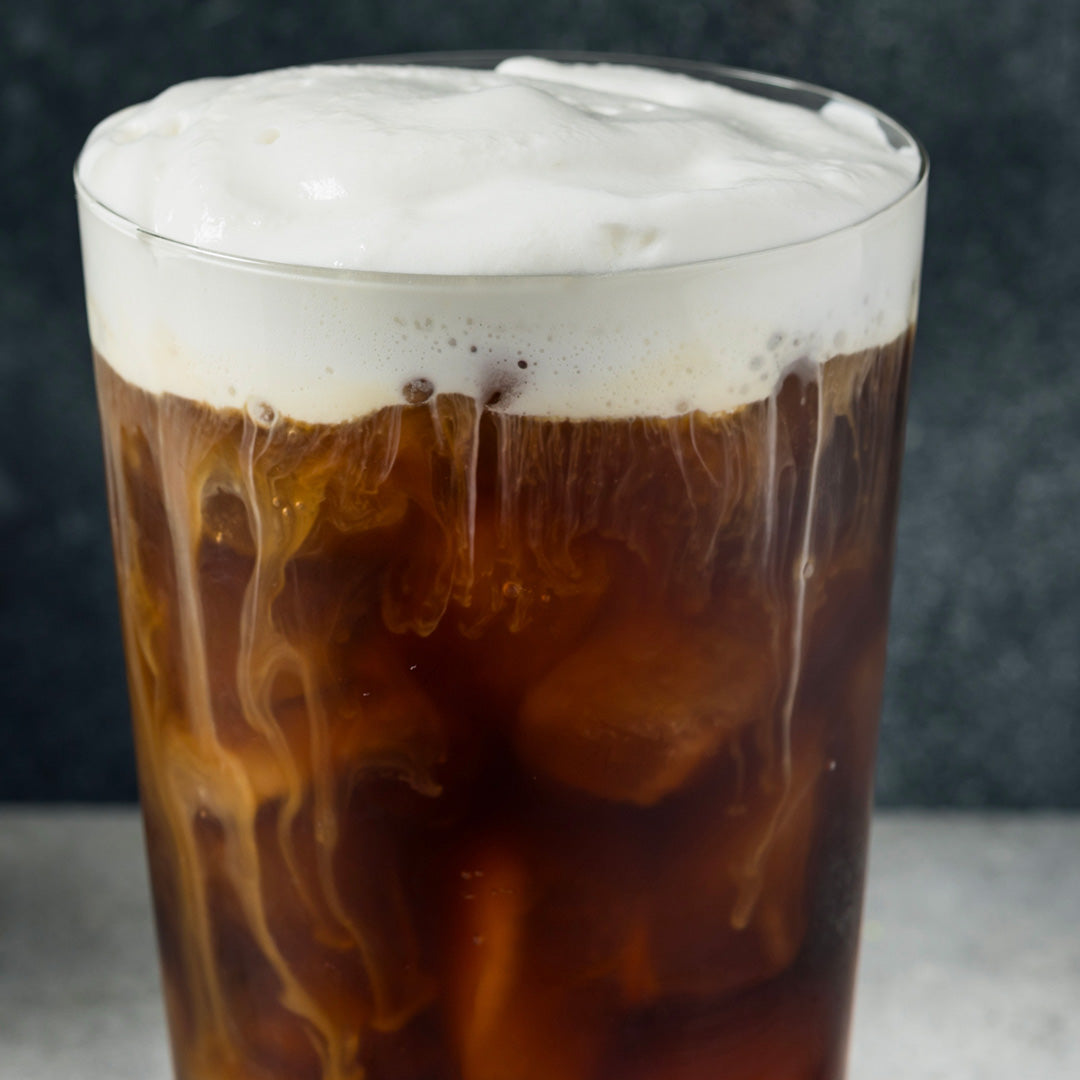 Glass of iced coffee with a thick layer of foam on a dark background
