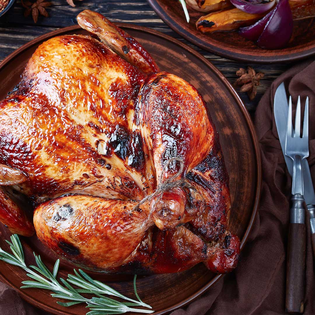 Roasted turkey on a wooden plate with rosemary and cutlery in the background