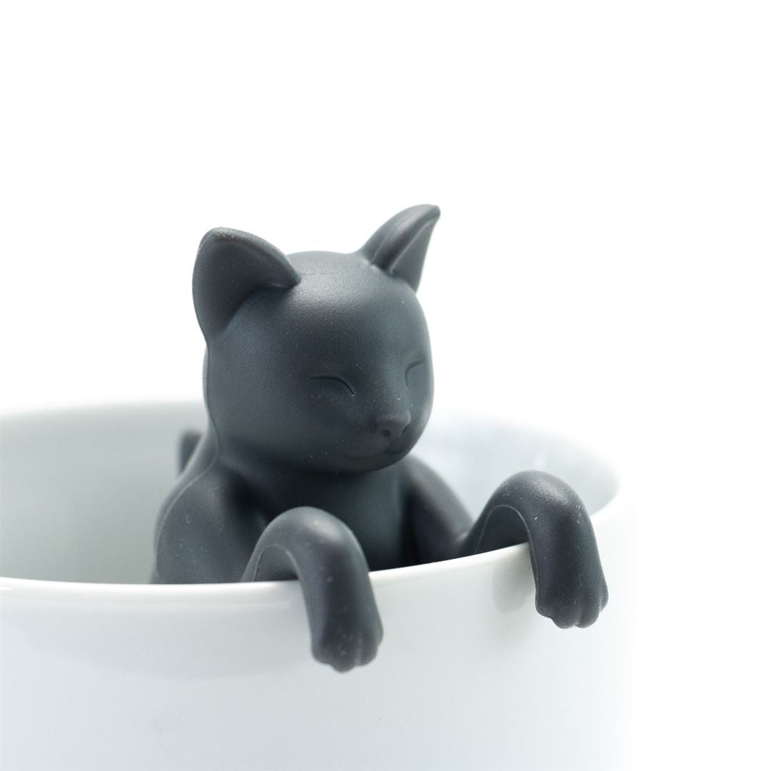 The Cat Infuser, made of BPA-free silicone, is a black cat that sits on the rim of a white cup with its front paws draped over and eyes closed for a relaxed look.